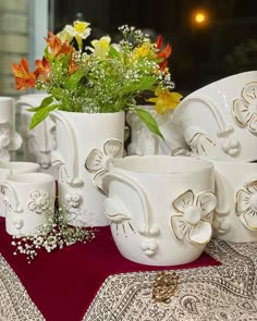 a table topped with white cups and vases filled with flowers