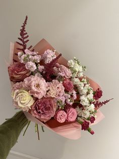 a bouquet of pink and white flowers is held up by someone's hand on the wall