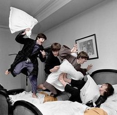 four boys jumping in the air over a bed with pillows on top of them and one boy holding up a pillow