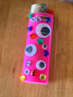 a pink lighter with lots of different colored buttons on the top and bottom, sitting on a wooden surface