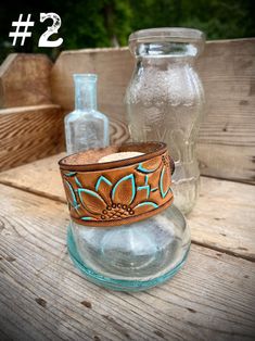 two glass jars sitting on top of a wooden table next to each other and one has a leather band around it