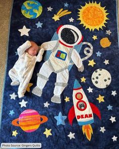 a baby laying on top of a blue blanket next to an astronaut themed wall hanging