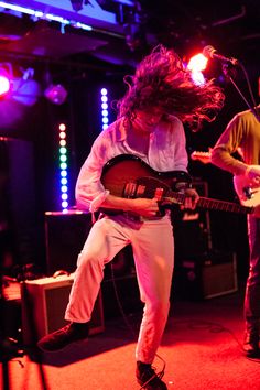 a man with long hair playing an electric guitar in front of two other men on stage