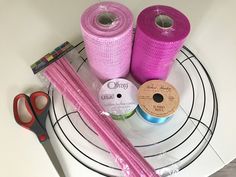 two spools of pink thread and some scissors on a white plate with wire