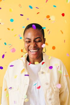 a woman standing in front of a yellow wall with confetti on it