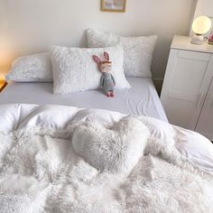 a white bed topped with pillows and a stuffed animal on it's headboard