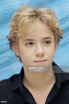 a young boy with blonde hair and black shirt looking at the camera, close up