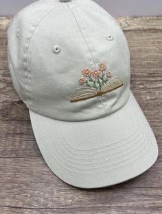 a white hat with flowers embroidered on the front and an open book in the back