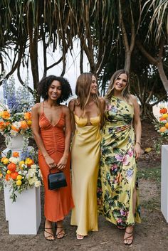 three beautiful women standing next to each other in front of some flowers and vases