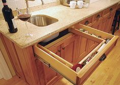 an open drawer in the middle of a kitchen counter next to a sink and wine bottle