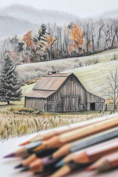 some colored pencils are sitting next to a drawing of a barn and trees with mountains in the background