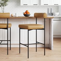 two stools in front of a kitchen island with fruit on it and a bowl of oranges