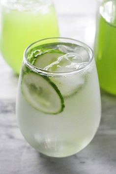 two glasses filled with ice and limeade on top of a marble table next to each other