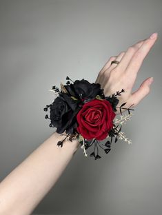 a woman's hand holding a red and black rose wrist corsage