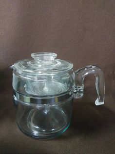 a clear glass teapot with a lid and handle on a brown surface, next to a black background