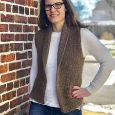 a woman leaning against a brick wall with her hands on her hips and wearing glasses