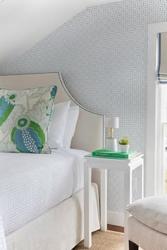 a white bed sitting under a window next to a chair and table in a bedroom