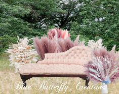 an old couch with flowers and feathers on it in the middle of a grassy field