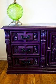 a purple dresser sitting on top of a wooden floor next to a green glass vase