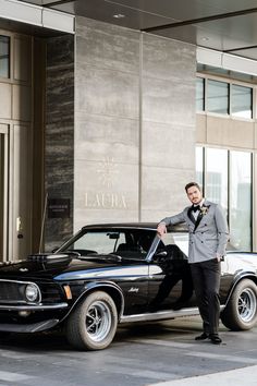 a man in a tuxedo standing next to a classic car