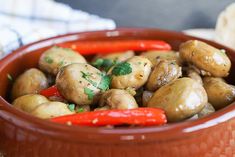 a red bowl filled with mushrooms and peppers on top of a wooden table next to bread