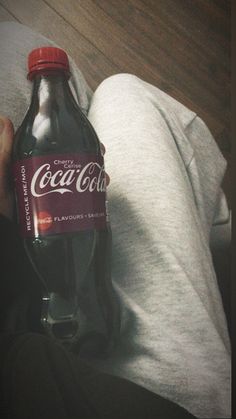 a bottle of coca cola sitting on top of a person's lap in front of a wooden floor