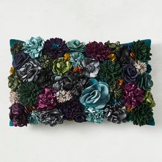 a decorative pillow made out of flowers on a white wall with blue and green accents