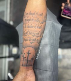 a man's arm with a cross and bible verse tattooed on the left forearm