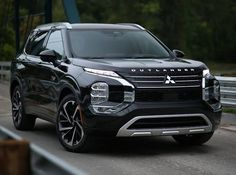 a black suv driving down a road next to a bridge with trees in the background