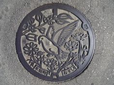 a manhole cover on the ground with a bird and flowers design painted on it