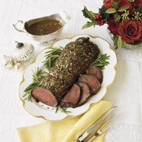 a white plate topped with sliced meat next to a bowl of soup and silverware