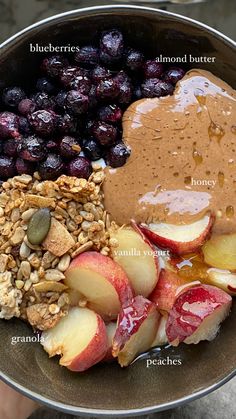 Close up of yogurt bowl with frozen blueberries, almond butter, honey, peaches and granola