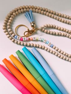 a wooden bead necklace with the word be kind spelled on it and six different colored markers