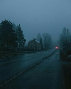 a foggy street with a red car on the road and houses in the background