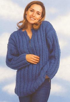 a woman wearing a blue sweater and jeans standing in front of the sky with her hands on her hips