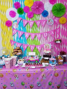 a birthday party with pink, blue and green decorations on the wall behind a cake table