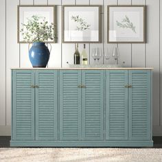 a blue cabinet with wine glasses and bottles on it in front of two framed pictures