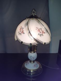 a table lamp that is sitting on top of a table next to a vase with flowers painted on it