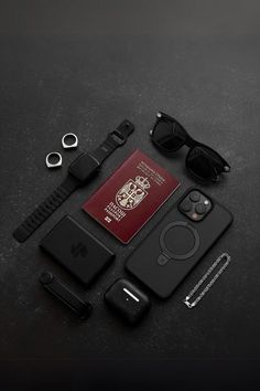 an apple watch, passport, sunglasses and other items laid out on a black surface