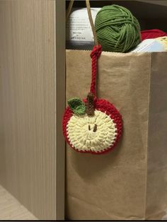 an apple ornament hanging from a brown paper bag with yarn on it's side