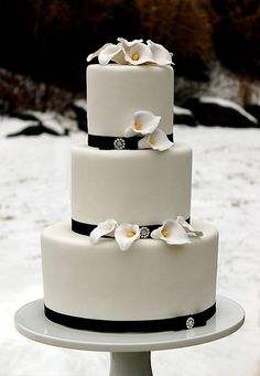 a three tiered cake with white flowers and black ribbon