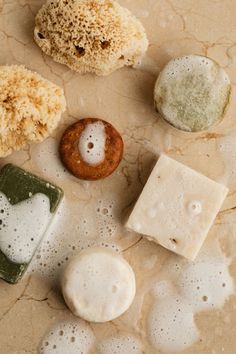 soaps and sponges are arranged on a marble surface with water droplets around them