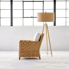 a wicker chair with two pillows on it in front of a floor lamp and large windows