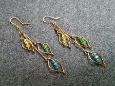 two pairs of gold earrings with green and blue stones on them sitting on a gray surface