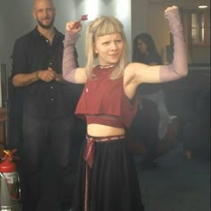 a woman in a red top and black skirt standing next to a man with his arms up