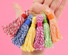 a hand holding several different colored tassels in it's palm, against a pink background