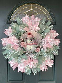 a pink and green christmas wreath with a snowman on it's front door