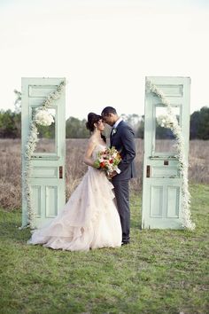 a bride and groom kissing in front of an open door with greenery on it