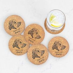 four cork coasters with dogs on them next to a drink glass and lemon wedge