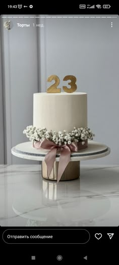 a white cake with gold numbers on top and pink ribbon around the bottom is sitting on a table